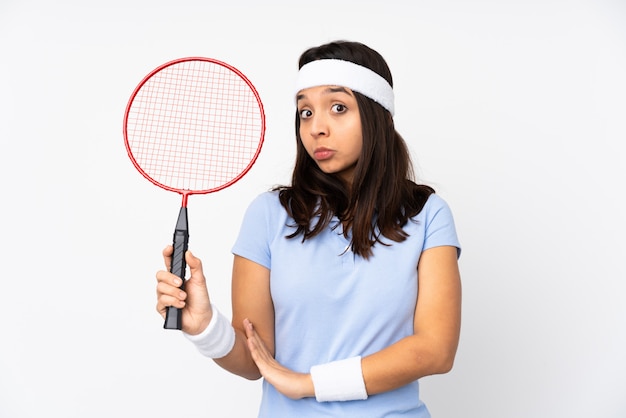 A mulher nova do jogador de badminton sobre a parede branca isolada que faz dúvidas gesticula ao levantar os ombros