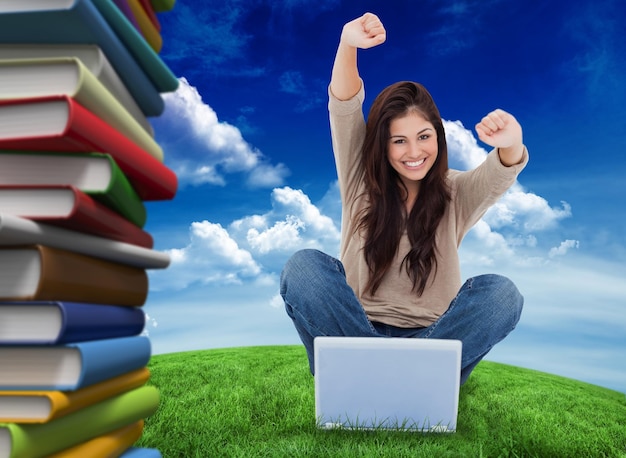 Foto a mulher olha para a frente enquanto comemora na frente de seu laptop contra um campo verde sob o céu azul