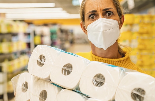 A mulher parece chocada com as compras de máscara facial no supermercado comprando papel higiênico de pânico se preparando para uma pandemia. Coronavírus COVID-19 teme prateleiras vazias em pânico em todo o mundo
