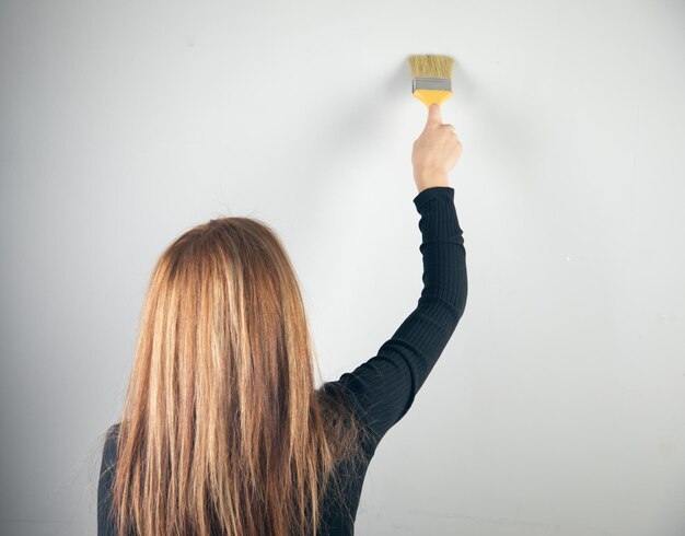 A mulher pintando uma parede com um pincel.