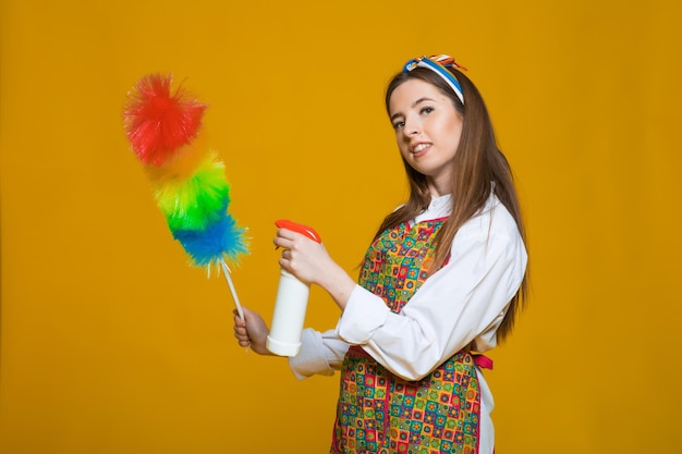 A mulher pinup segura uma mulher pinup de espanador de garrafa de sopa com cara feliz em fundo amarelo