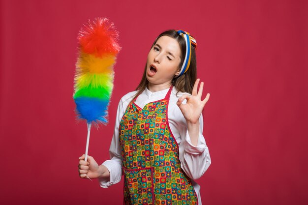 A mulher pinup segura uma mulher pinup de espanador de garrafa de sopa com cara feliz no fundo rosa