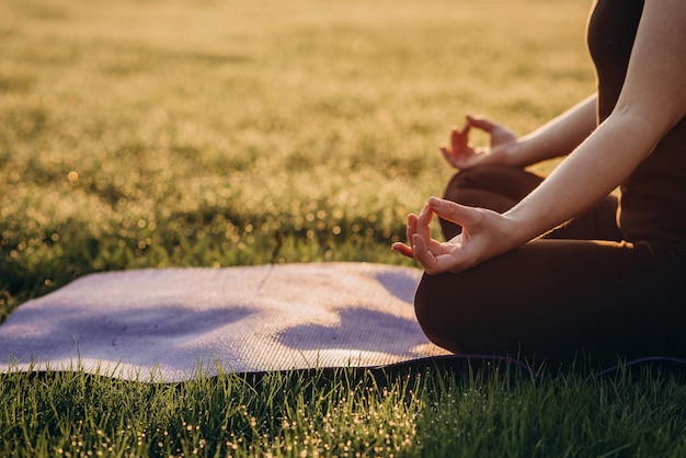 A mulher pratica a ioga na posição de lótus em uma manhã ensolarada na grama com foco seletivo macio do orvalho. Copie o espaço.