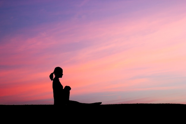 A mulher praticando Spinal twist yoga coloca ao ar livre sobre o fundo do céu do por do sol.