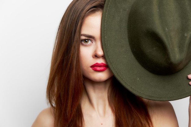 A mulher que guarda o chapéu cobre seus ombros nus do rosto perto dos lábios vermelhos do rosto