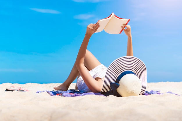 A mulher que lê um livro na praia tropical com relaxa no tempo de férias.