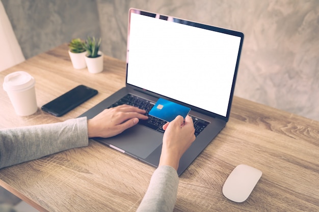 A mulher que usa o computador portátil atividade on-line paga o cartão de crédito na tabela de madeira.