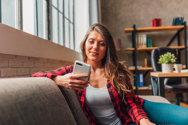 A mulher relaxa em casa em seu tempo livre com telefone celular