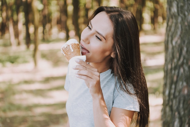 A mulher satisfeita nova come o gelado na floresta.