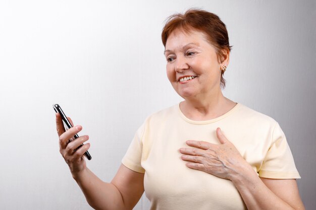 Foto a mulher sênior olha o telefone em branco em uma camiseta leve