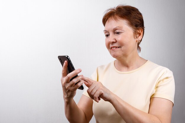 A mulher sênior olha o telefone em branco em uma camiseta leve