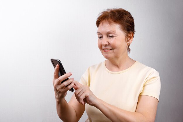 A mulher sênior olha o telefone em branco em uma camiseta leve