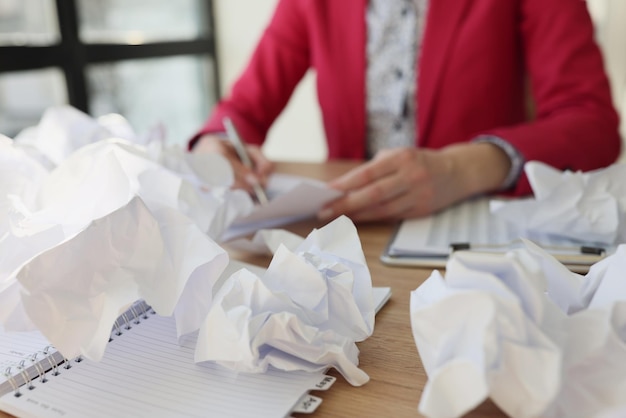 A mulher senta-se à mesa de madeira perto de folhas de papel amassadas espalhadas na mesa no escritório feminino