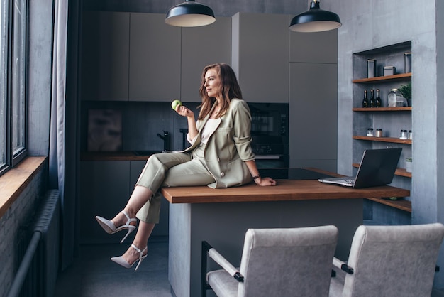 A mulher senta-se na cozinha com uma maçã durante uma pausa