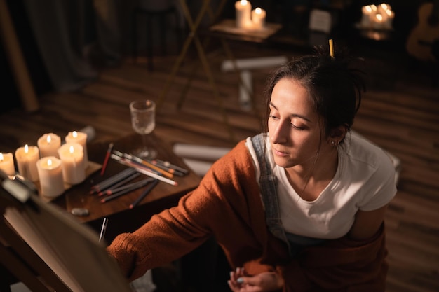 A mulher senta-se no meio da sala em meio a desenhos e velas fracassados espalhados