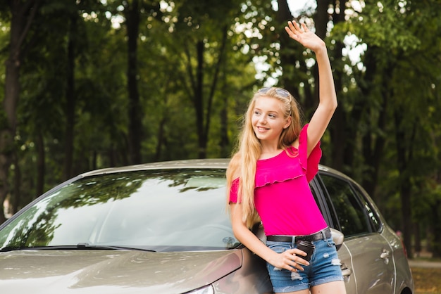 A mulher sorri e cumprimenta com a mão perto do carro