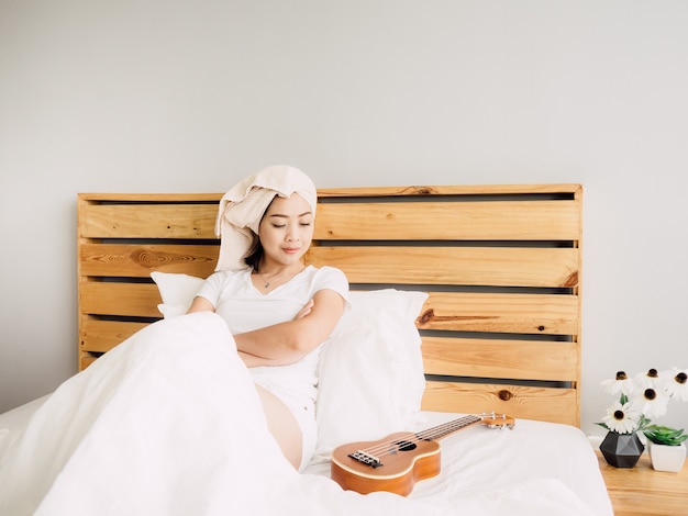 A mulher tem um dia bem relaxar com seu ukulele na cama.