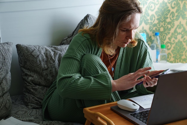 A mulher trabalha em um laptop em casa na cama trabalhando em licença médica