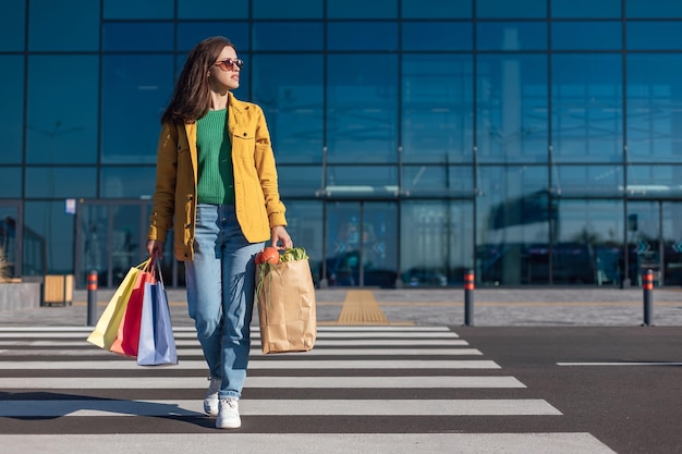 A mulher vai na faixa de pedestres de um shopping com sacolas de compras com mantimentos