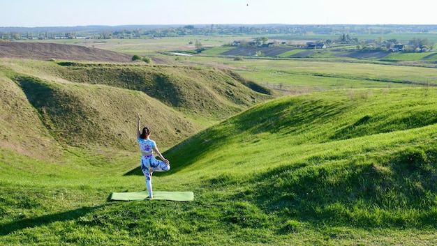 A mulher vai para a aptidão de ioga esportiva na natureza na primavera no verão em um dia ensolarado Pessoa mostrando suas costas em pose de ioga Corpo feminino saudável em roupas esportivas