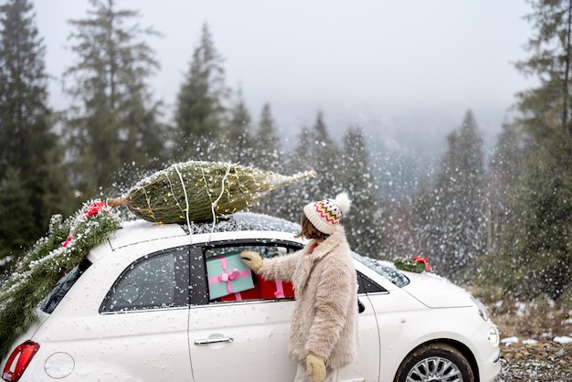 A mulher viaja de carro com presentes e árvore de natal na estrada da montanha