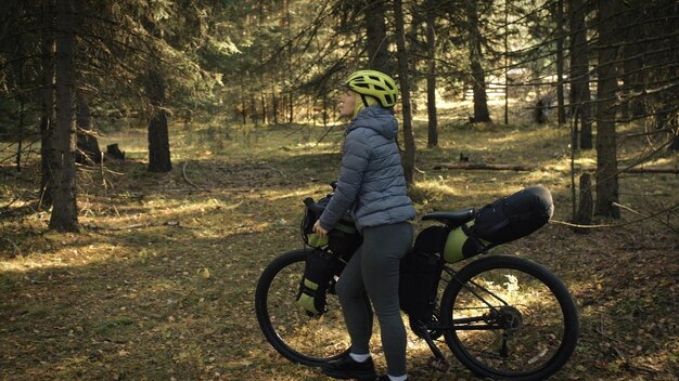 A mulher viaja em ciclismo de terreno misto com bike bikepacking ao ar livre A viagem do viajante com bolsas de bicicleta Elegante bikepacking bike sportswear nas cores pretas verdes Magic forest park