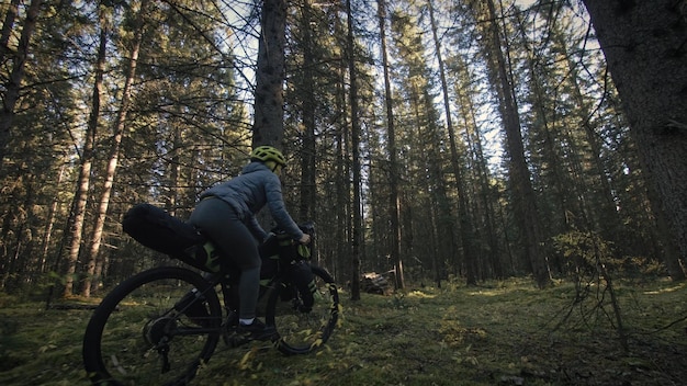 A mulher viaja em ciclismo de terreno misto com bike bikepacking ao ar livre A viagem do viajante com bolsas de bicicleta Elegante bikepacking bike sportswear nas cores pretas verdes Magic forest park