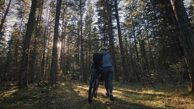 A mulher viaja em terreno misto cicloturismo com bike bikepacking ao ar livre A viagem do viajante com bolsas de bicicleta Elegante bikepacking bike sportswear nas cores pretas verdes Magic forest park
