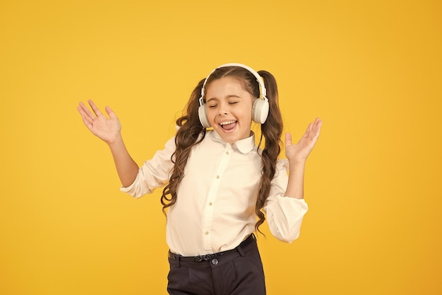 A música combina com seu humor Adorável garotinha cantando uma música em fundo amarelo Criança pequena bonita ouvindo música tocando em fones de ouvido Curtindo sua música favorita