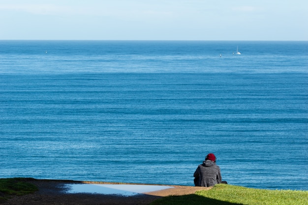 A música de escuta do homem novo está sentando-se na borda do penhasco do mar.