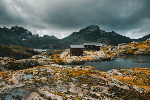 A natureza dura das ilhas Lofoten da Noruega. Outono paisagem de montanha. Caminhe até o Monte Munken, casas de madeira, um abrigo à beira do lago contra um céu tempestuoso.