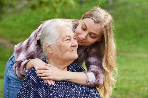 Foto a neta adulta abraça a avó por trás sorri olha para ela