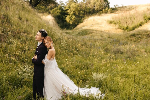 A noiva abraça um elegante noivo bonito Lindo casal na natureza no contexto das colinas