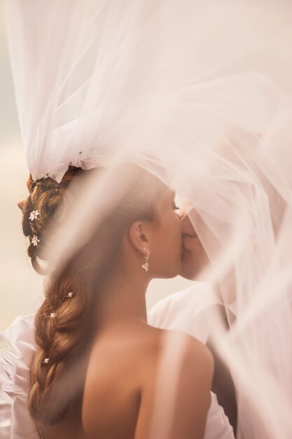 A noiva beija o noivo sob o véu penteado de casamento da noiva