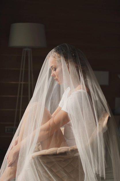 A noiva coberta com um véu senta-se em uma cadeira no hotel