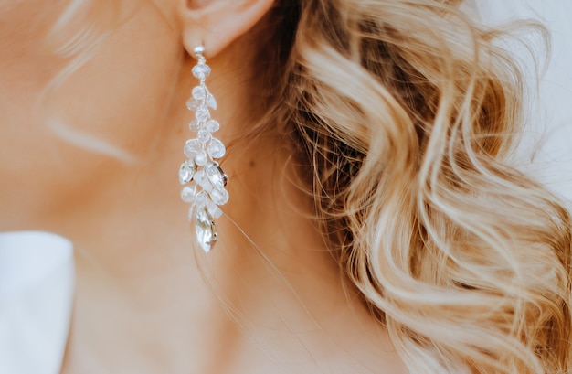 A noiva coloca lindos brincos de casamento. Menina com penteado com cachos usando acessórios de joias