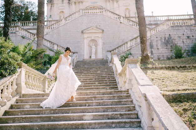 A noiva com grinalda desce as escadas pitorescas do antigo templo em vista traseira prcanj
