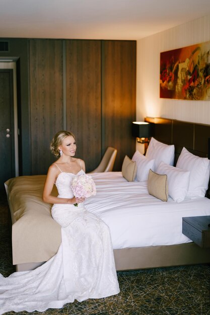 Foto a noiva com um buquê senta-se numa cama dupla e olha para outro lado.