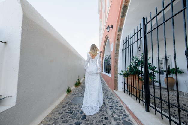A noiva de mulheres bonitas de cabelos loiros azul em um vestido sexy longo branco de casamento em Santorini na Grécia