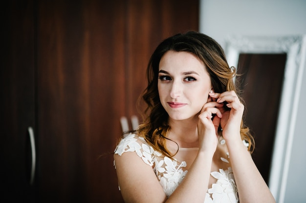 Foto a noiva de vestido branco usa brincos de ouro com pérolas. nas mãos da noiva decoração em forma de brinco. manhã de casamento. joalheria. feche a maquiagem.