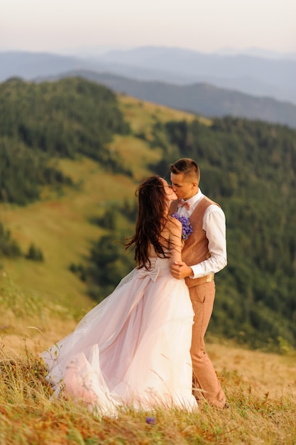 A noiva e o noivo beijam em um fundo de montanhas de outono. Pôr do sol. Fotografia de casamento.