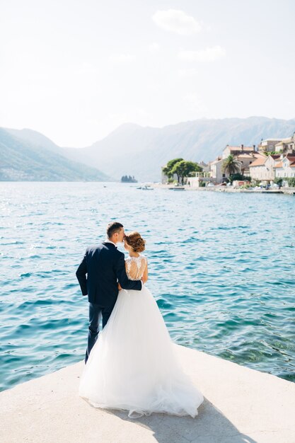 A noiva e o noivo estão abraçados e se beijando no cais perto da cidade velha de perast.