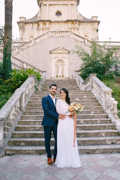 Foto a noiva e o noivo estão abraçados perto das escadas da igreja da natividade da virgem prcanj