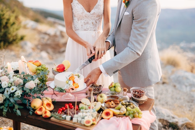 A noiva e o noivo estão cortando um bolo durante uma mesa de bufê após a cerimônia de casamento no monte