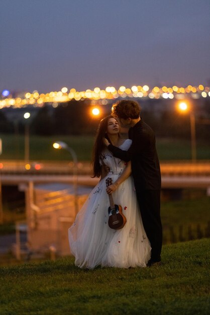 Foto a noiva e o noivo estão em uma colina em frente às luzes iluminadas da cidade.