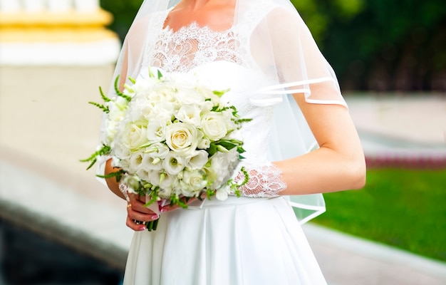 A noiva em um lindo vestido branco tem nas mãos um lindo buquê de rosas brancas e eustomas