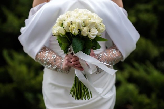 A noiva em um vestido de noiva branco está segurando um buquê de flores brancas peônias rosas Casamento Noiva e noivo Delicado buquê de boas-vindas Linda decoração de casamentos com folhas