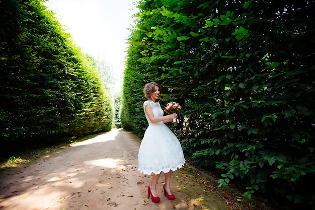 A noiva em um vestido de noiva branco segura um buquê em uma parede do parque verde