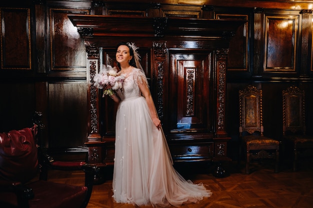 A noiva em um vestido de noiva e com um buquê está no antigo interior do castelo.