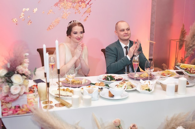 A noiva feliz e o noivo engraçado sentam-se à mesa e celebram o casamento no salão de banquetes